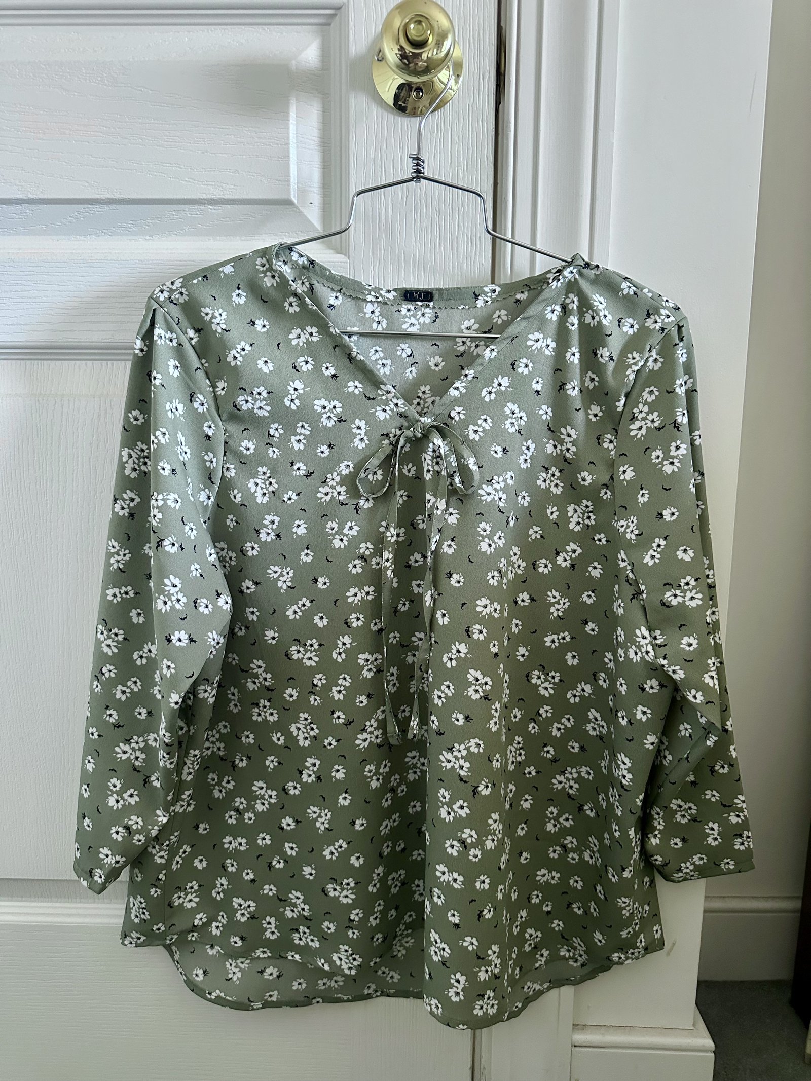 Sage floral chiffon blouse with bow neckline on a hanger